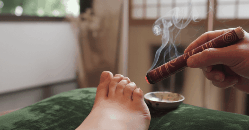 Burning moxibustion stick held near outer pinky toe acupuncture point BL67 to support breech babyturning with controlled heat