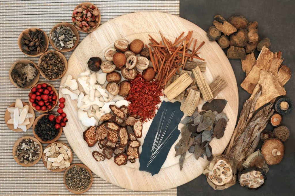Assorted Chinese herbs, dried botanicals, mushrooms, roots, and acupuncture needles arranged on a wooden tray